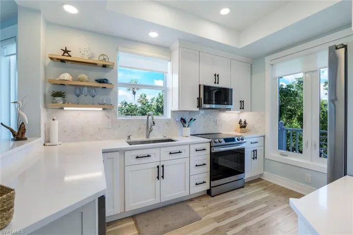 Kitchen featuring white cabinetry, tasteful backsplash, appliances with stainless steel finishes, open shelves, and light wood-style floors