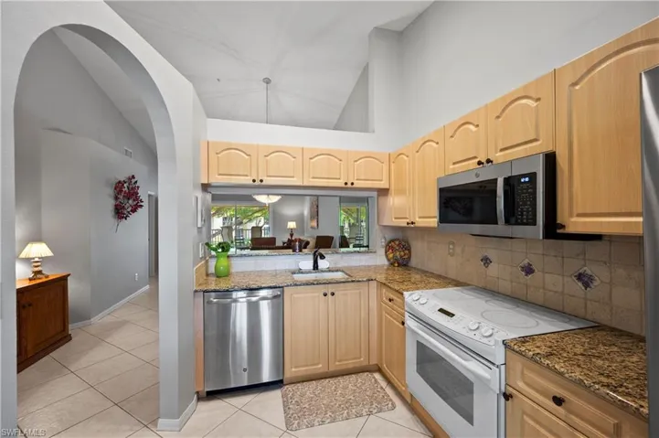 Kitchen featuring appliances with stainless steel finishes, light brown cabinetry, backsplash, light tile patterned floors, and high vaulted ceiling