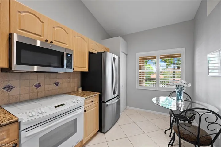Kitchen featuring appliances with stainless steel finishes, backsplash, vaulted ceiling, light stone counters, and light brown cabinetry