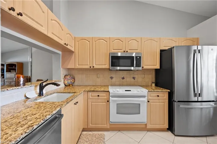 Kitchen featuring appliances with stainless steel finishes, light brown cabinetry, light tile patterned floors, light stone counters, and high vaulted ceiling