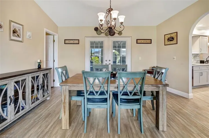 Dining space featuring a notable chandelier, french doors, lofted ceiling and arched entry to kitchen