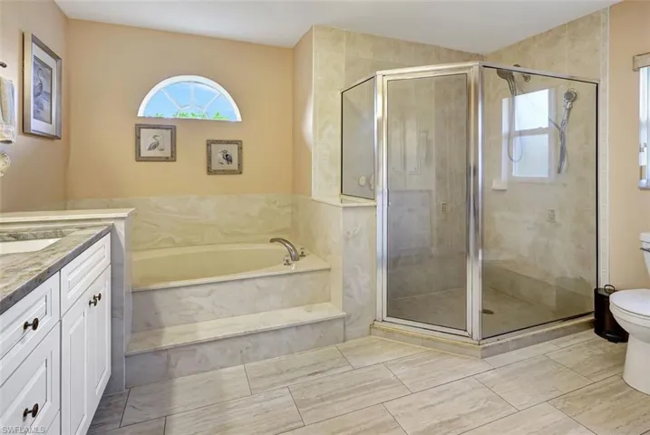 Primary bathroom featuring porcelian tile flooring, garden soaking tub, plus walk in shower, vanity, and toilet