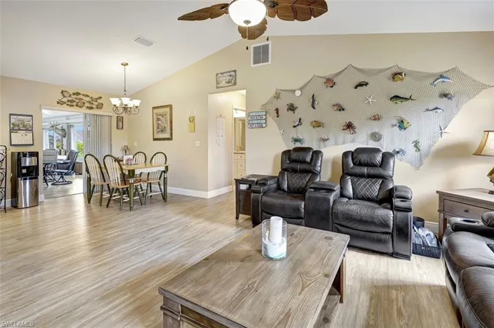 Family room featuring ceiling fan with notable chandelier, vaulted ceiling, and light wood-type flooring