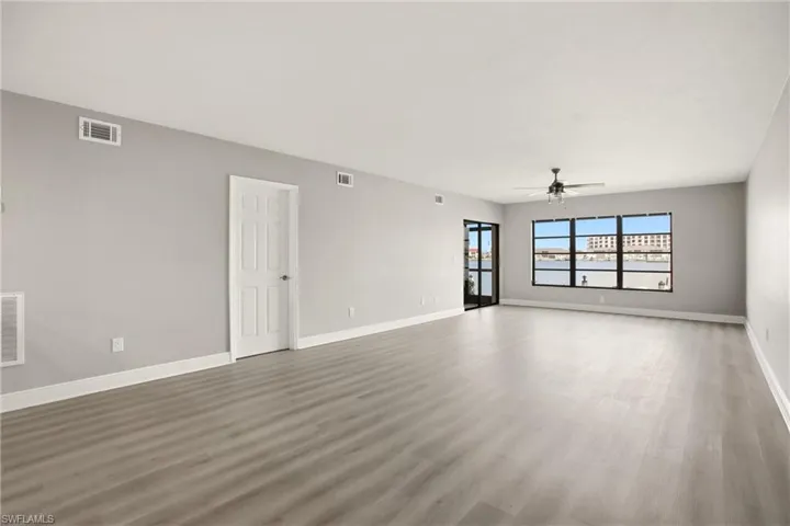Expansive room featuring wood-finish flooring, a large multi-pane window, a ceiling fan, and a glass-paneled door