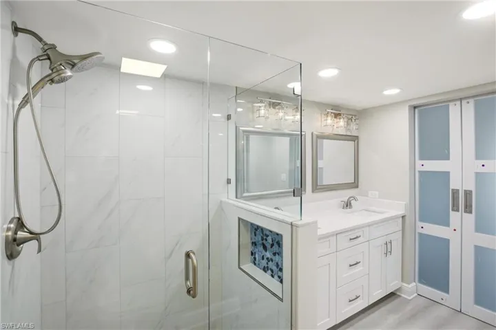 Glass-enclosed shower with a brushed nickel shower system and white tiled walls