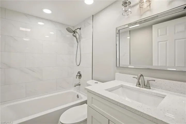 Full bathroom featuring a white bathtub with a wall-mounted showerhead, white subway tile surround, white vanity with an integrated sink, brushed nickel faucet, and a large mirrored vanity cabinet