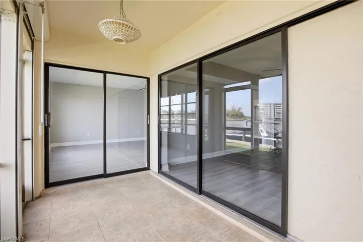 Tiled outdoor area featuring two sets of expansive sliding glass doors, a textured overhead light fixture, and a neutral wall finish