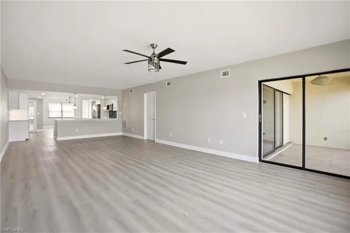 Spacious living area featuring light wood-finish flooring, a contemporary ceiling fan, and sliding glass doors to an outdoor patio