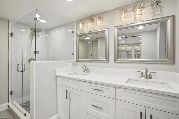 Dual vanity with white cabinetry and integrated sinks, complemented by a glass-enclosed shower featuring a tiled surround and mosaic floor