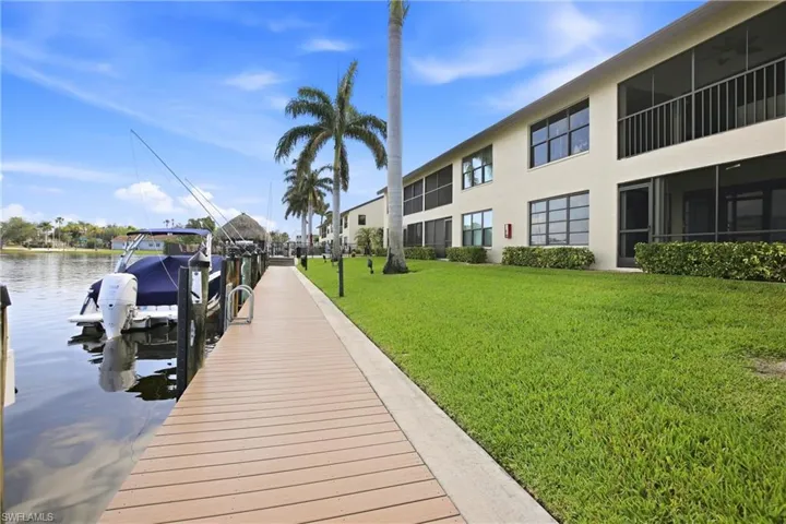 Waterfront property featuring a composite dock, a stucco exterior building, screened porches, mature palm trees, and a manicured lawn