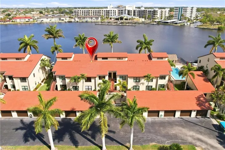 Waterfront community featuring multiple buildings with red tile roofs, a communal pool, and private garages