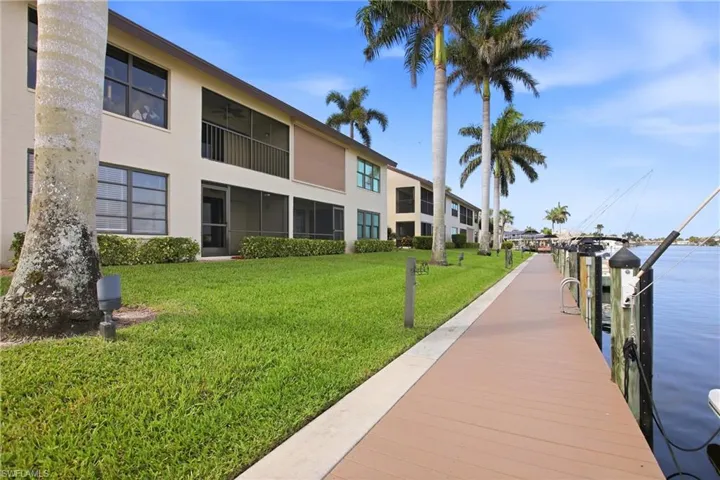 Waterfront property featuring a long dock, boat slips on request, multiple boat slips, and a manicured lawn with palm trees