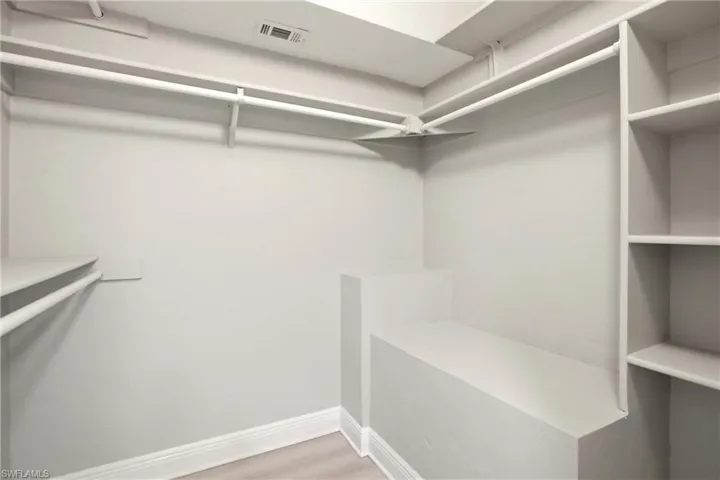 Walk-in closet featuring built-in shelving, multiple hanging rods, corner bench, and light wood-finish flooring