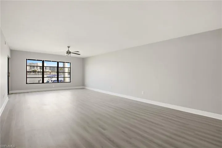 Spacious interior featuring light wood-finish flooring, a contemporary ceiling fan, and large windows with black framing