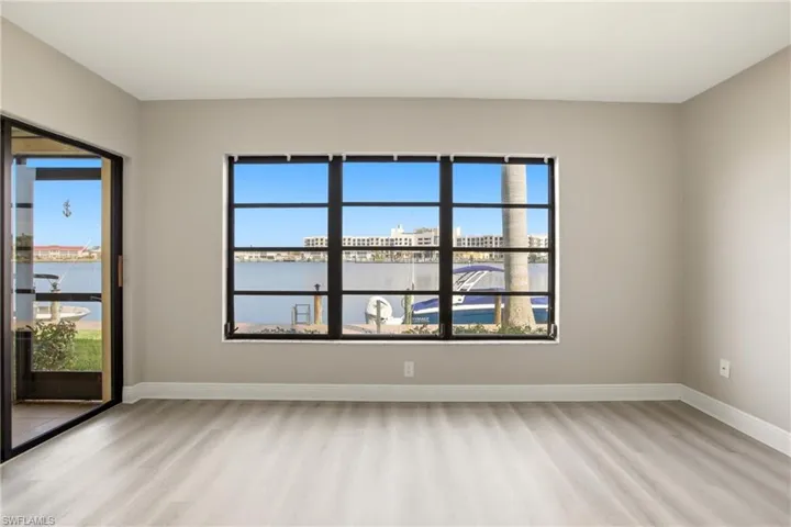 Waterfront room featuring a large picture window, a sliding glass door, light wood-finish flooring, white baseboards, and neutral wall paint