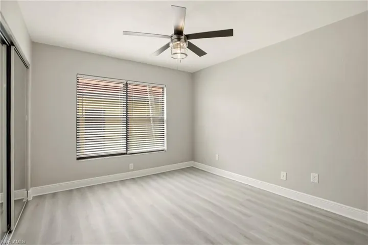 Spacious room featuring wood-finish flooring, a contemporary ceiling fan with integrated lighting, a large window with blinds, and light-toned wall paint