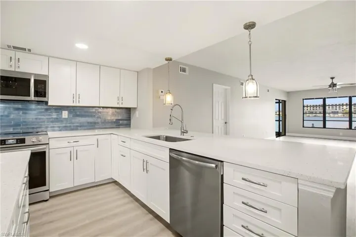 Kitchen featuring white shaker-style cabinetry, stainless steel appliances, a blue subway tile backsplash, and light-toned countertops