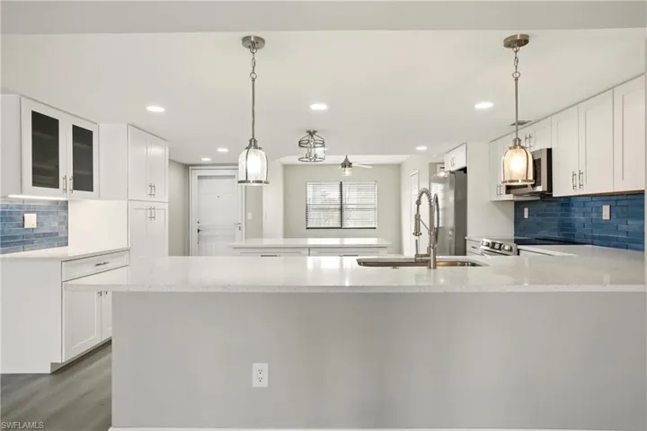 Modern kitchen featuring white shaker cabinetry, light-toned countertops, a blue subway tile backsplash, and stainless steel appliances