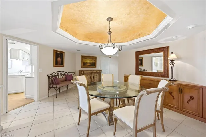 Recessed ceiling with decorative finish, crown molding, white tile flooring, and a cased opening to an additional room