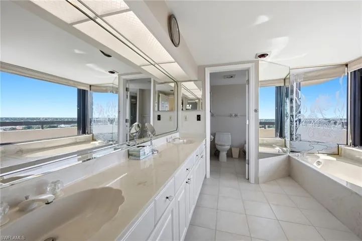 Expansive bathroom featuring a dual vanity, integrated sinks, a built-in soaking tub, tile flooring, and mirror accents