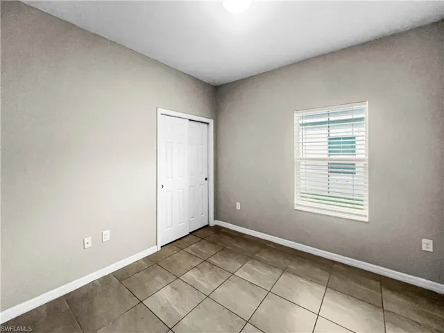 Neutral-toned walls complement the tile flooring in this room featuring a window with blinds and a bi-fold closet door