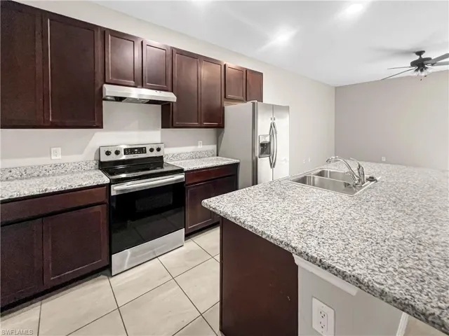 Kitchen featuring dark wood cabinetry, light speckled countertops, stainless steel appliances, and a central island with an integrated double sink