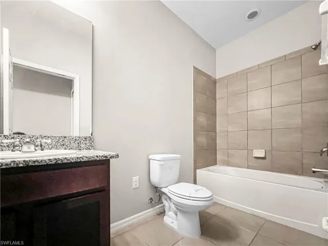 Bathroom featuring a dark wood-finish vanity with a granite-style countertop, a white porcelain sink with chrome fixtures, and a frameless mirror
