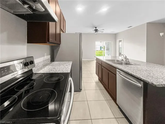 Kitchen featuring granite-style countertops, stainless steel appliances, dark wood-finish cabinetry, and tile flooring