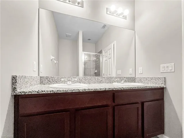 Dual vanity featuring granite countertops with integrated sinks, dark wood-finish cabinetry, and contemporary lighting fixtures