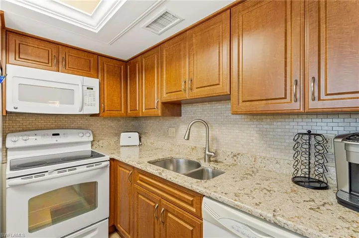 Kitchen featuring white stove and microwave. Beautiful brown cabinets, and a double sink.
