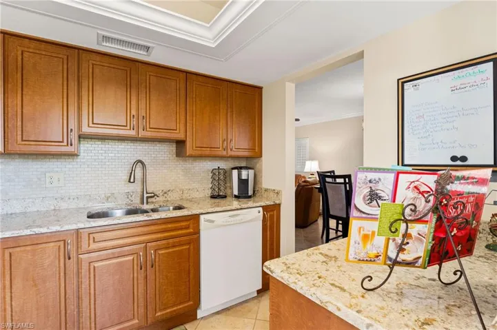 Kitchen featuring light granite counters, decorative backsplash, white dishwasher, and a double sink