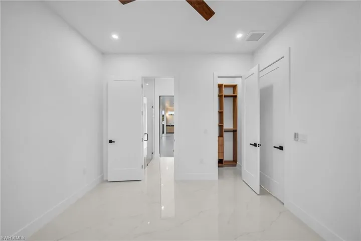 Unfurnished bedroom featuring a spacious closet, light marble finish flooring, recessed lighting, and ceiling fan