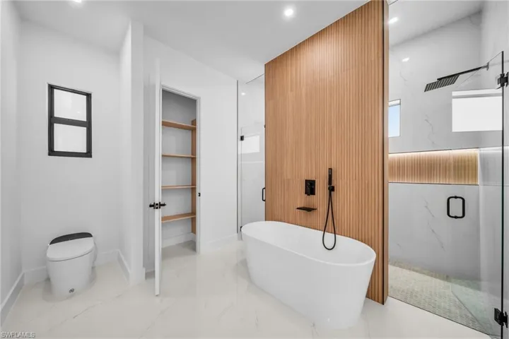 Bathroom featuring a marble finish shower, marble tiled floors, a freestanding bath, a spacious closet, and recessed lighting