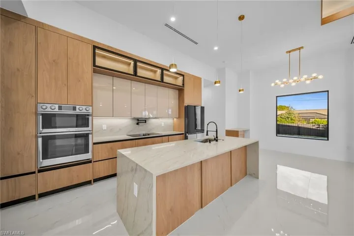 Kitchen with light stone counters, modern cabinets, decorative light fixtures, decorative backsplash, and an island with sink