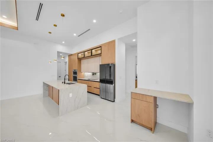 Kitchen with light brown cabinets, pendant lighting, light stone counters, freestanding refrigerator, and light marble finish floors