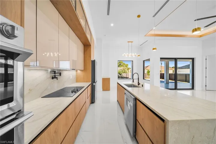 Kitchen with modern cabinets, light stone counters, black appliances, a large island, and decorative light fixtures