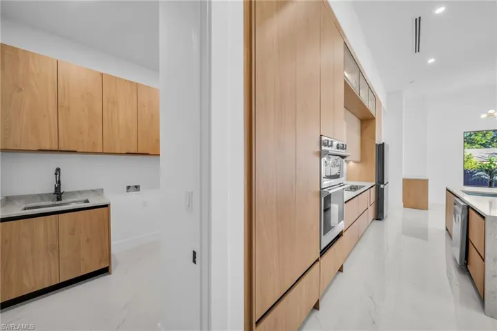 Kitchen featuring modern cabinets, light marble finish floors, light stone countertops, recessed lighting, and appliances with stainless steel finishes