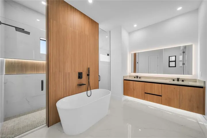 Full bathroom featuring a marble finish shower, light marble finish flooring, double vanity, recessed lighting, and a freestanding bath
