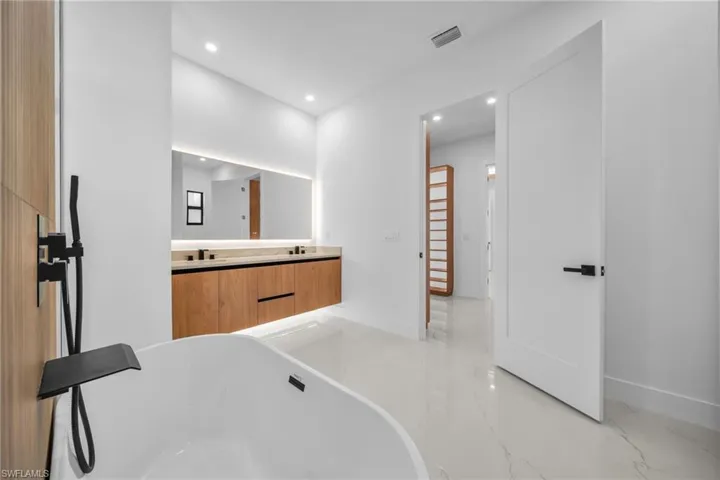 Bathroom featuring double vanity, a freestanding bath, light marble finish floors, and recessed lighting