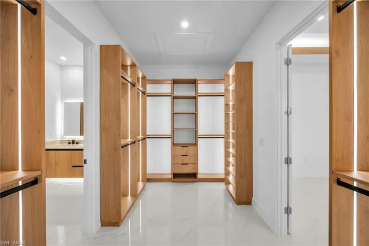Spacious closet featuring light marble finish flooring, a barn door, and attic access