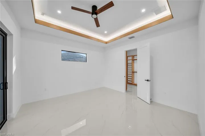 Spare room featuring a raised ceiling, light marble finish floors, ceiling fan, and recessed lighting