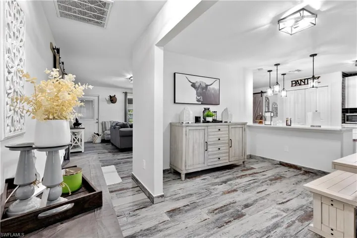 Kitchen with light hardwood / wood-style floors, decorative light fixtures, stainless steel microwave, and kitchen peninsula