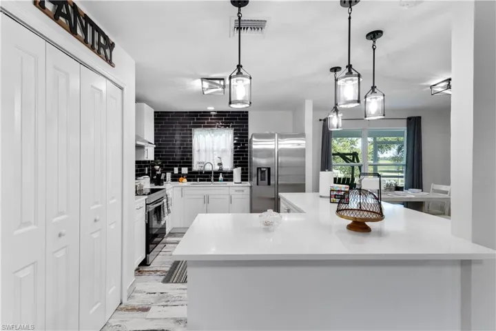 Kitchen featuring tasteful backsplash, stainless steel appliances, pendant lighting, white cabinets, and light wood-type flooring