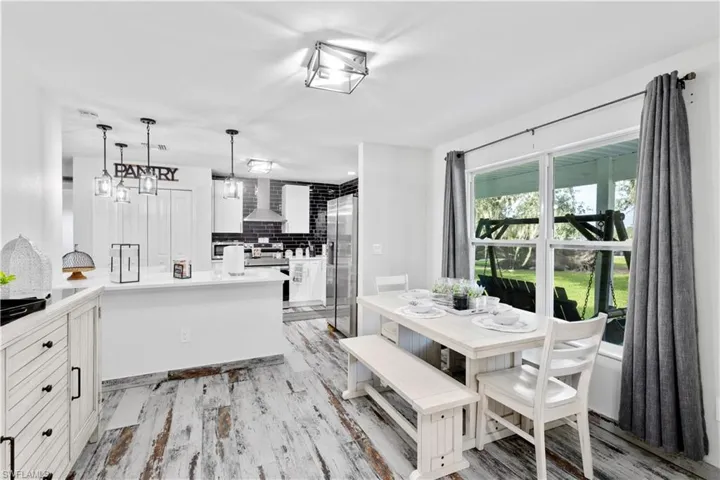 Kitchen with tasteful backsplash, light wood-type flooring, kitchen peninsula, white cabinets, and wall chimney exhaust hood