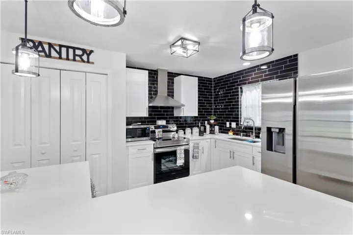 Kitchen featuring stainless steel appliances, white cabinets, wall chimney range hood, sink, and decorative light fixtures