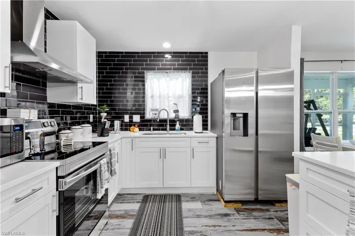 Kitchen featuring white cabinetry, wall chimney range hood, backsplash, appliances with stainless steel finishes, and sink