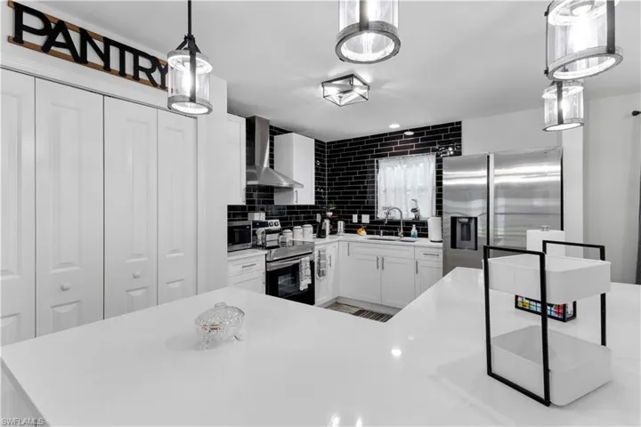Kitchen with stainless steel appliances, white cabinets, wall chimney range hood, pendant lighting, and decorative backsplash