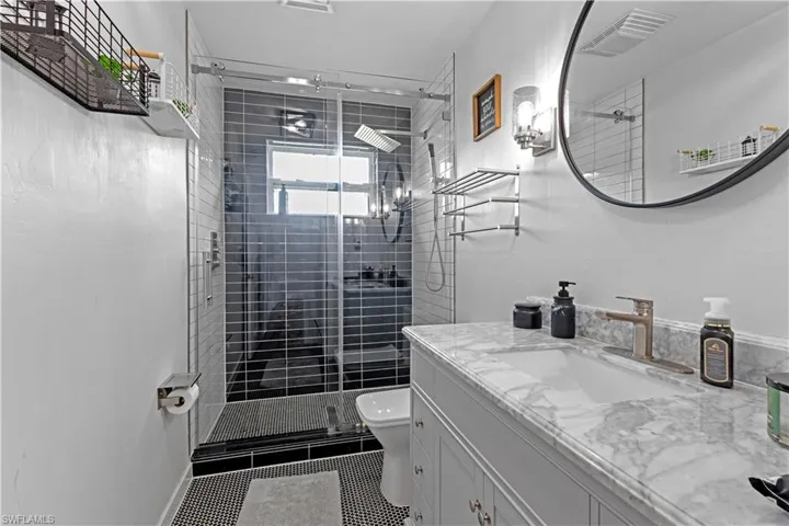 Bathroom with a shower with door, vanity, tile patterned floors, and toilet
