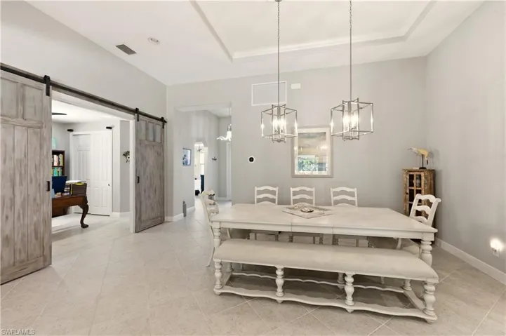 Dining area featuring a barn door, a raised ceiling, light tile patterned floors, and an office area