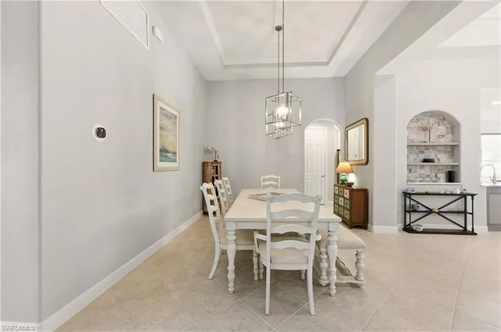 Dining space with arched walkways, light tile patterned floors, a raised ceiling, and built in features
